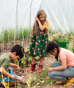 Little Green Radicals green orange blooms repeat print reversible pinny kids dress being worn with a yellow t-short underneath and red wellington boots.