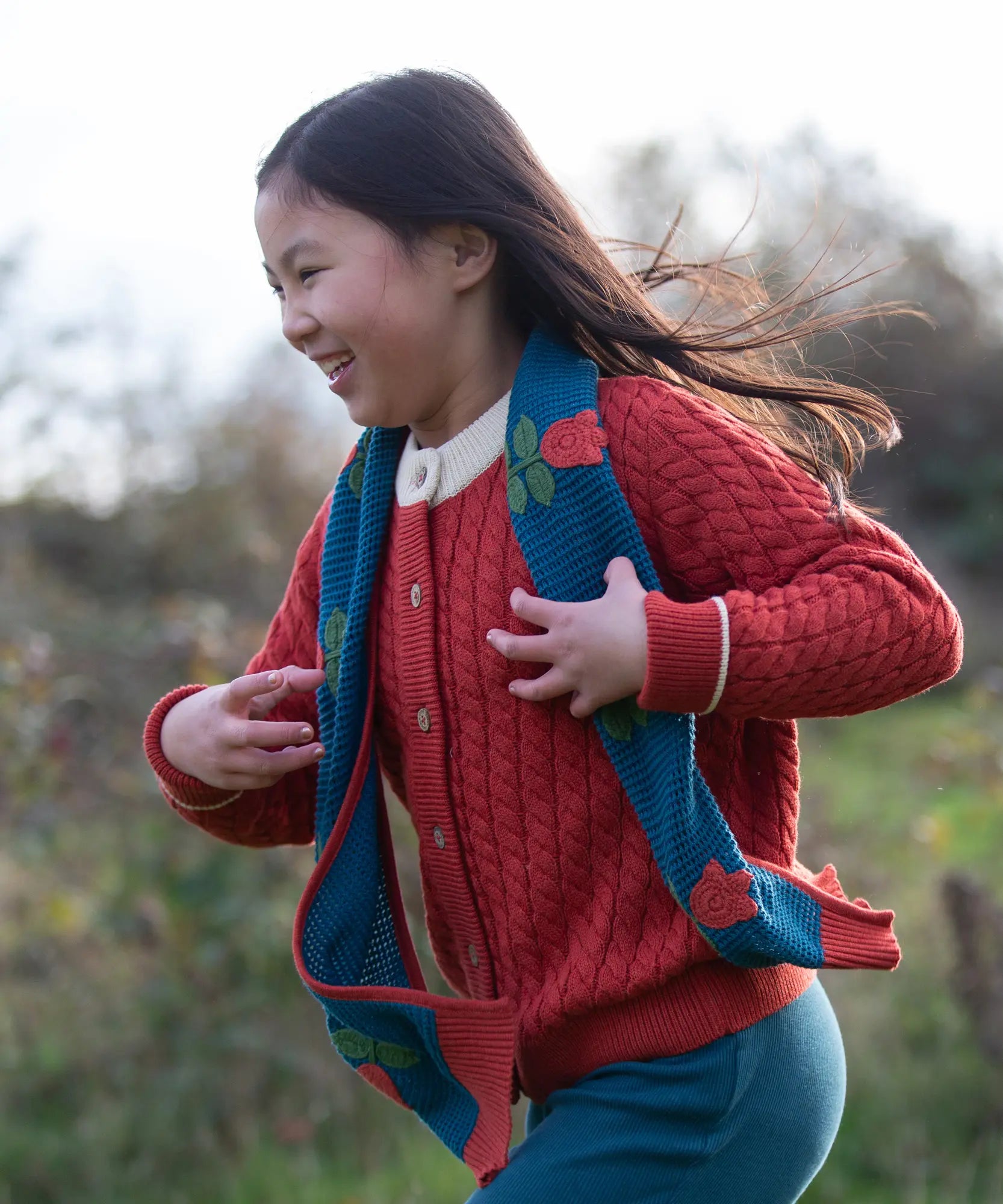 Child wearing Little Green Radicals tulips knitted blue scarf. Blue scarf with red tulips.