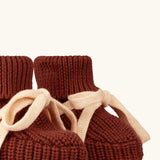 Close up of the Little Green Radicals hazelnut rust brown organic cotton knitted baby booties with cream coloured ties. 