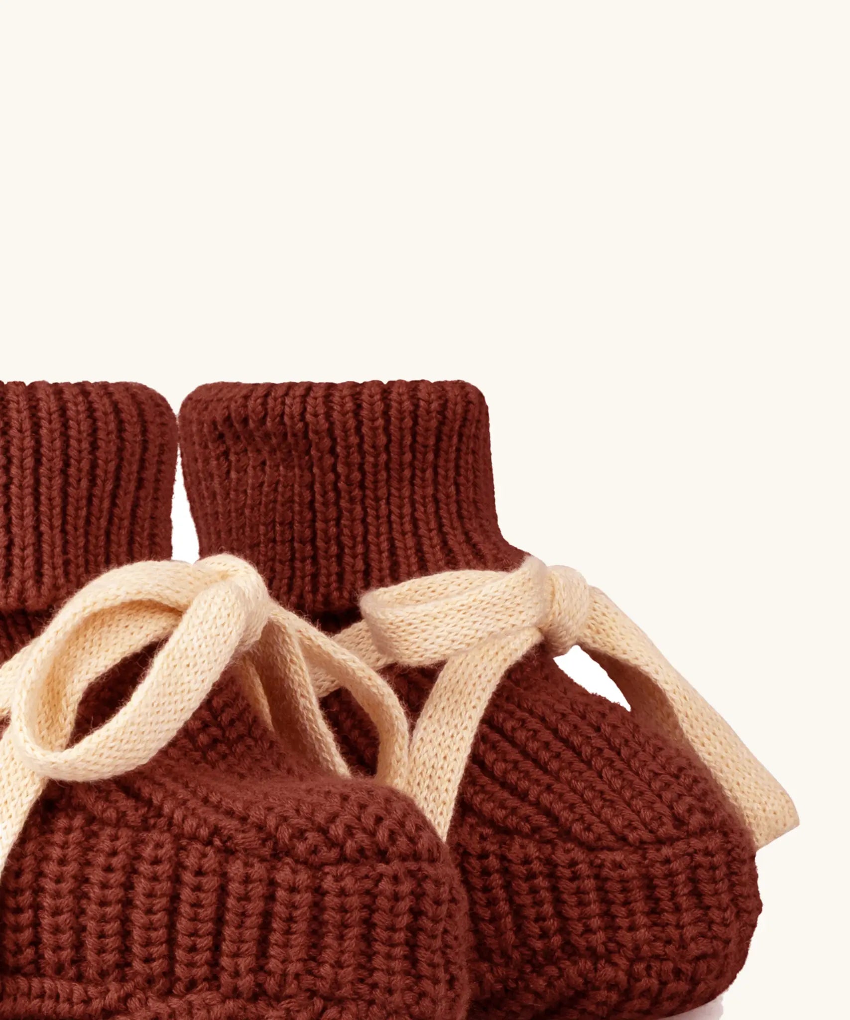 Close up of the Little Green Radicals hazelnut rust brown organic cotton knitted baby booties with cream coloured ties. 