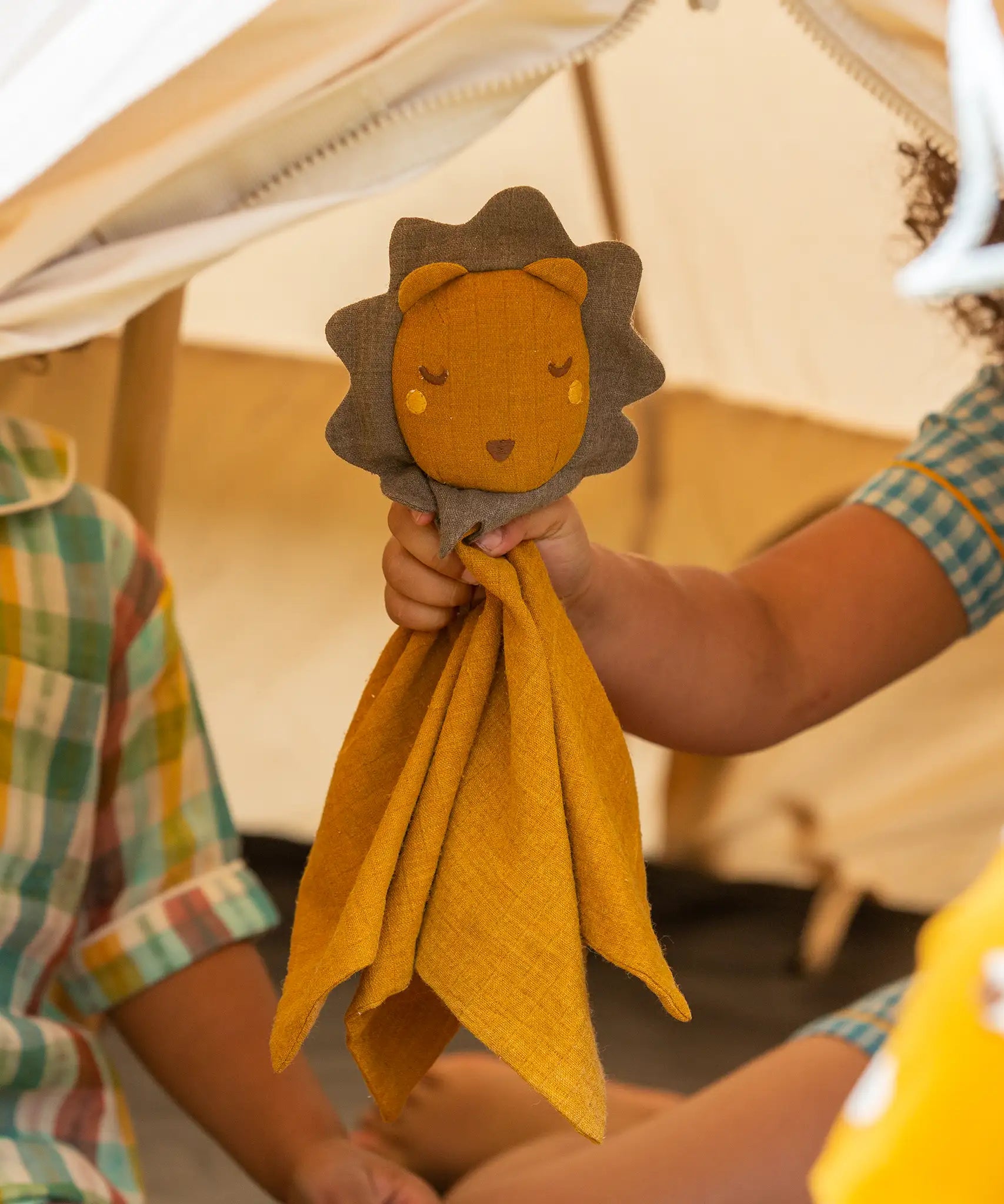 A child holding the Little Green Radicals Golden yellow Lion Organic Cotton Baby Comforter Toy up to the camera.
