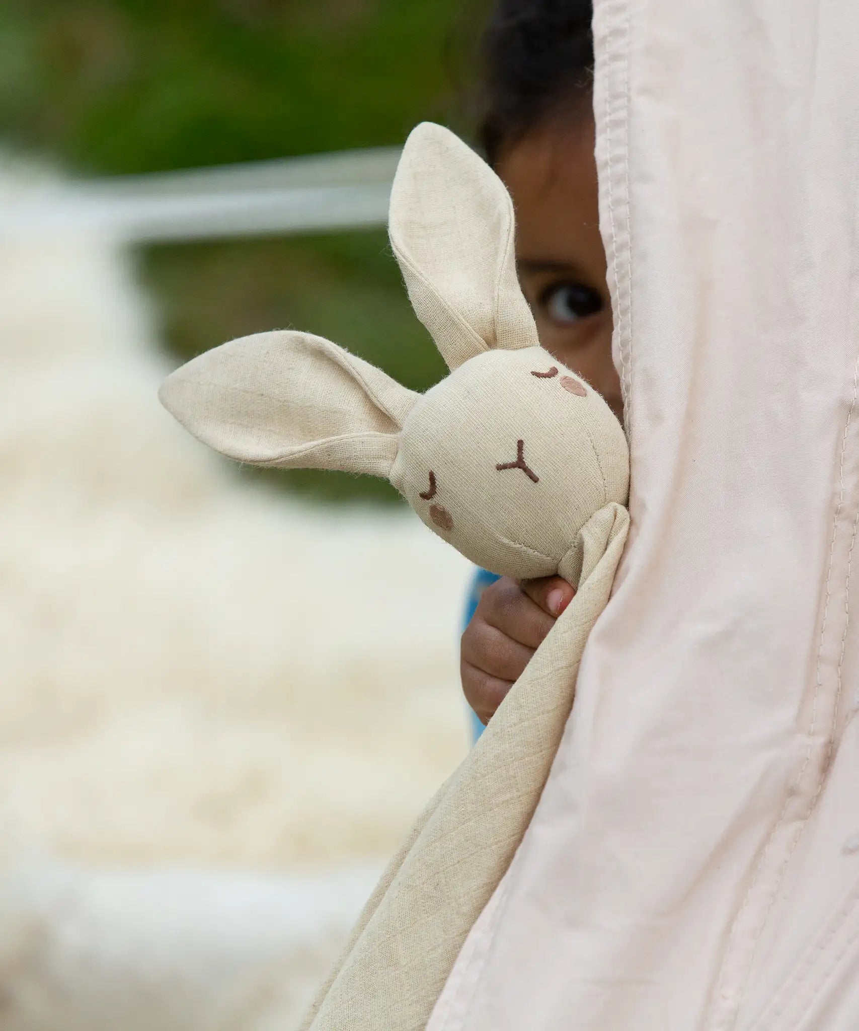A child playing peek-a-boo holding the Little Green Radicals rabbit organic cotton baby comforter toy in front of them.