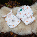 Little Green Radicals moon and sun classic pyjama set shown folded and placed on a sheepskin rug. A GOTS organic cotton pyjama set including a long sleeve shirt style top in light pink with prints of cute birds flying through stars the moon and sun also includes matching bottoms. These pyjamas are part of a wide range of organic cotton clothing for children available here at Babipur.