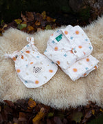 Little Green Radicals moon and sun classic pyjama set shown folded and placed on a sheepskin rug. A GOTS organic cotton pyjama set including a long sleeve shirt style top in light pink with prints of cute birds flying through stars the moon and sun also includes matching bottoms. These pyjamas are part of a wide range of organic cotton clothing for children available here at Babipur.