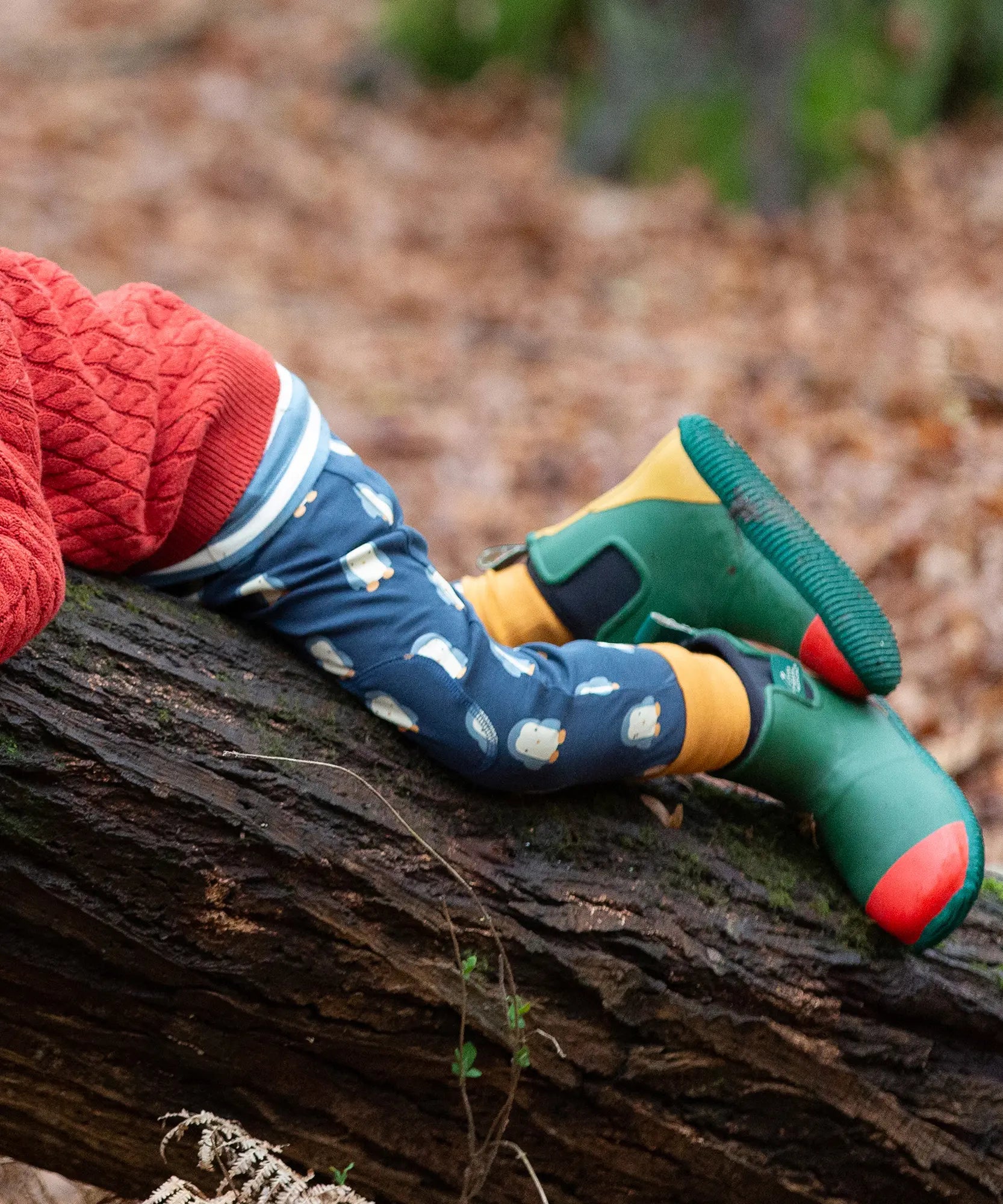 Child wearing Little Green Radicals organic cotton comfy joggers with a blue penguins design and green wellington boots.