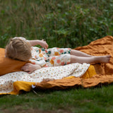 Child laying on a blanket outdoors wearing the Little Green Radicals organic cotton short pyjamas set in cream with a pink and yellow flora print. 