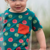 Close up of a child wearing the Little Green Radicals apple picking organic cotton playset outfit. A short sleeved t-shirt with red and green repeat apple print on a green background with green and cream striped joggers. 