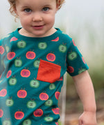 Close up of a child wearing the Little Green Radicals apple picking organic cotton playset outfit. A short sleeved t-shirt with red and green repeat apple print on a green background with green and cream striped joggers. 