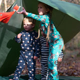Children standing outside a tent in the forest. They are all wearing Little Green Radicals organic cotton pyjamas. One is wearing a pair with the Winter Rabbit on them, one in wearing navy and white striped design and the third is wearing the sleeping sheep print. Little green Radicals have a wide range of organic cotton, Fairtrade children's clothing an outerwear available here at Babipur.