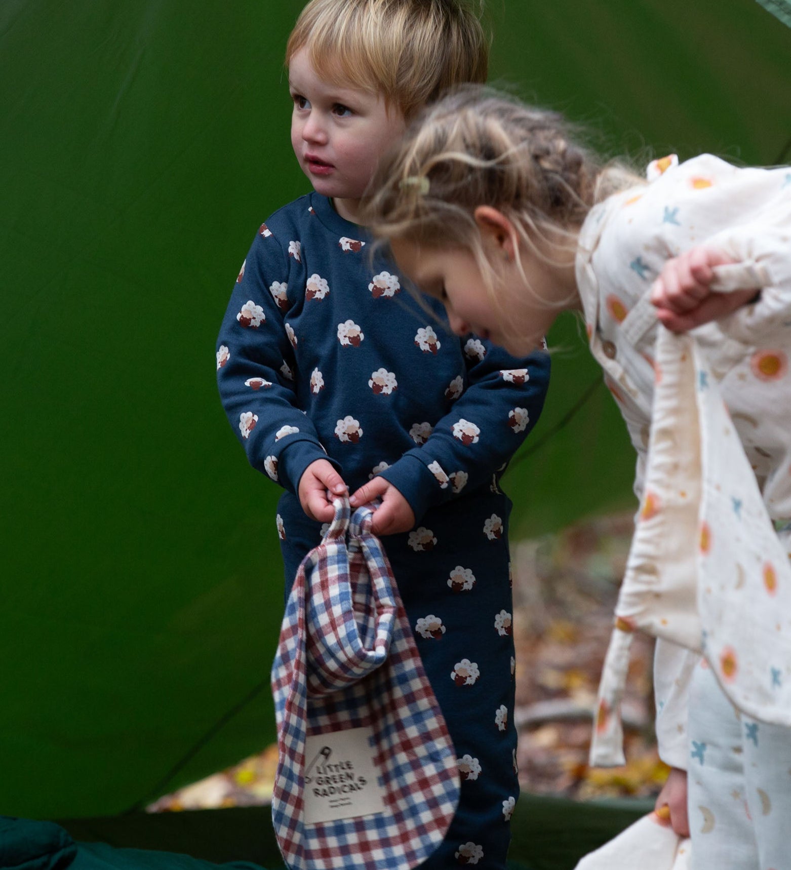 A child wearing the Little Green Radicals  Organic Cotton Sleeping Sheep print Pyjamas. Another child is standing besides them. Little green Radicals have a wide range of organic cotton, Fairtrade children's clothing an outerwear available here at Babipur.
