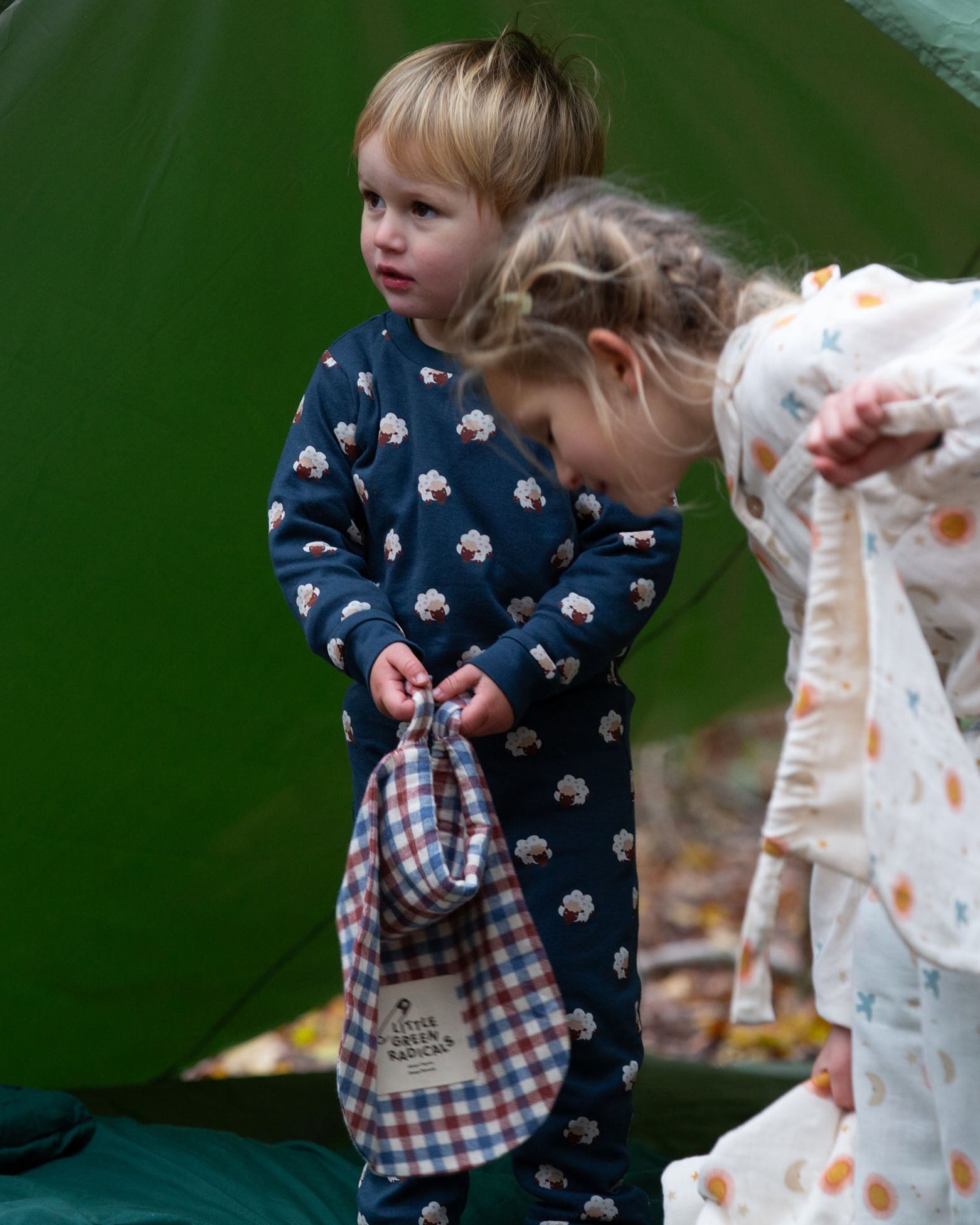 A child wearing the Little Green Radicals  Organic Cotton Sleeping Sheep print Pyjamas. Another child is standing besides them. Little green Radicals have a wide range of organic cotton, Fairtrade children's clothing an outerwear available here at Babipur.
