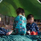 Children sitting in a tent in the forest. They are all wearing Little Green Radicals organic ccotton pyjamas. One is wearing a pair with the Winter Rabbit on them, one in wearing navy and white striped design and the third is wearing the sleeping sheep print. Little green Radicals have a wide range of organic cotton, Fairtrade children's clothing an outerwear available here at Babipur.