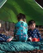Children sitting in a tent in the forest. They are all wearing Little Green Radicals organic ccotton pyjamas. One is wearing a pair with the Winter Rabbit on them, one in wearing navy and white striped design and the third is wearing the sleeping sheep print. Little green Radicals have a wide range of organic cotton, Fairtrade children's clothing an outerwear available here at Babipur.