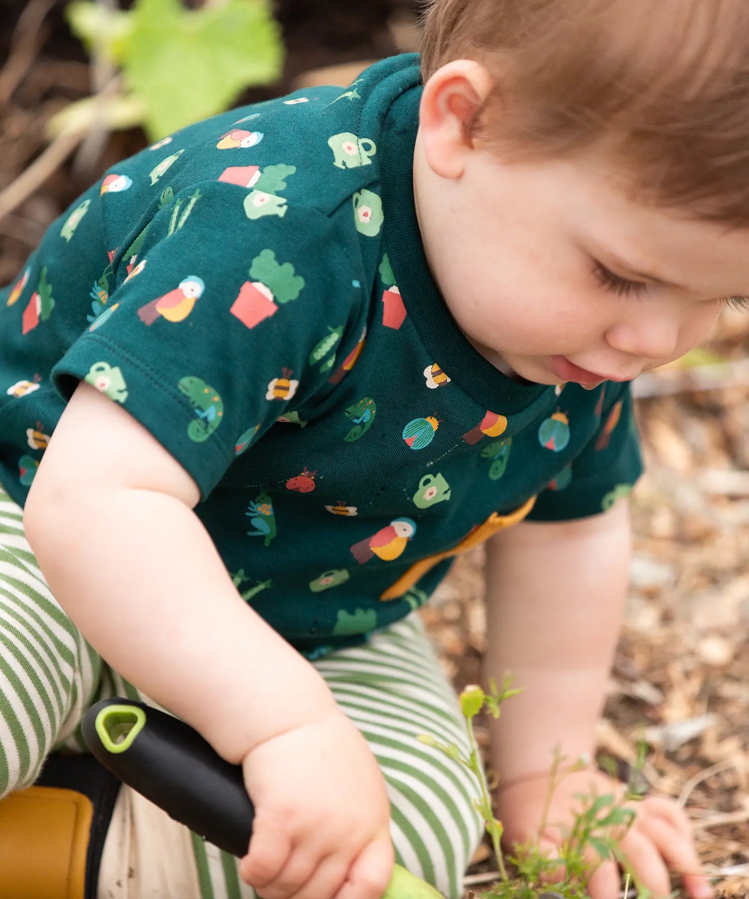 Child wearing the Little Green Radicals Spring garden organic cotton playset outfit. Repeat pattern green t-shirt and green and cream striped joggers. 