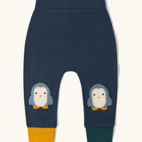 Little Green Radicals organic cotton penguin knee patch joggers with one yellow and one dark green leg cuff.