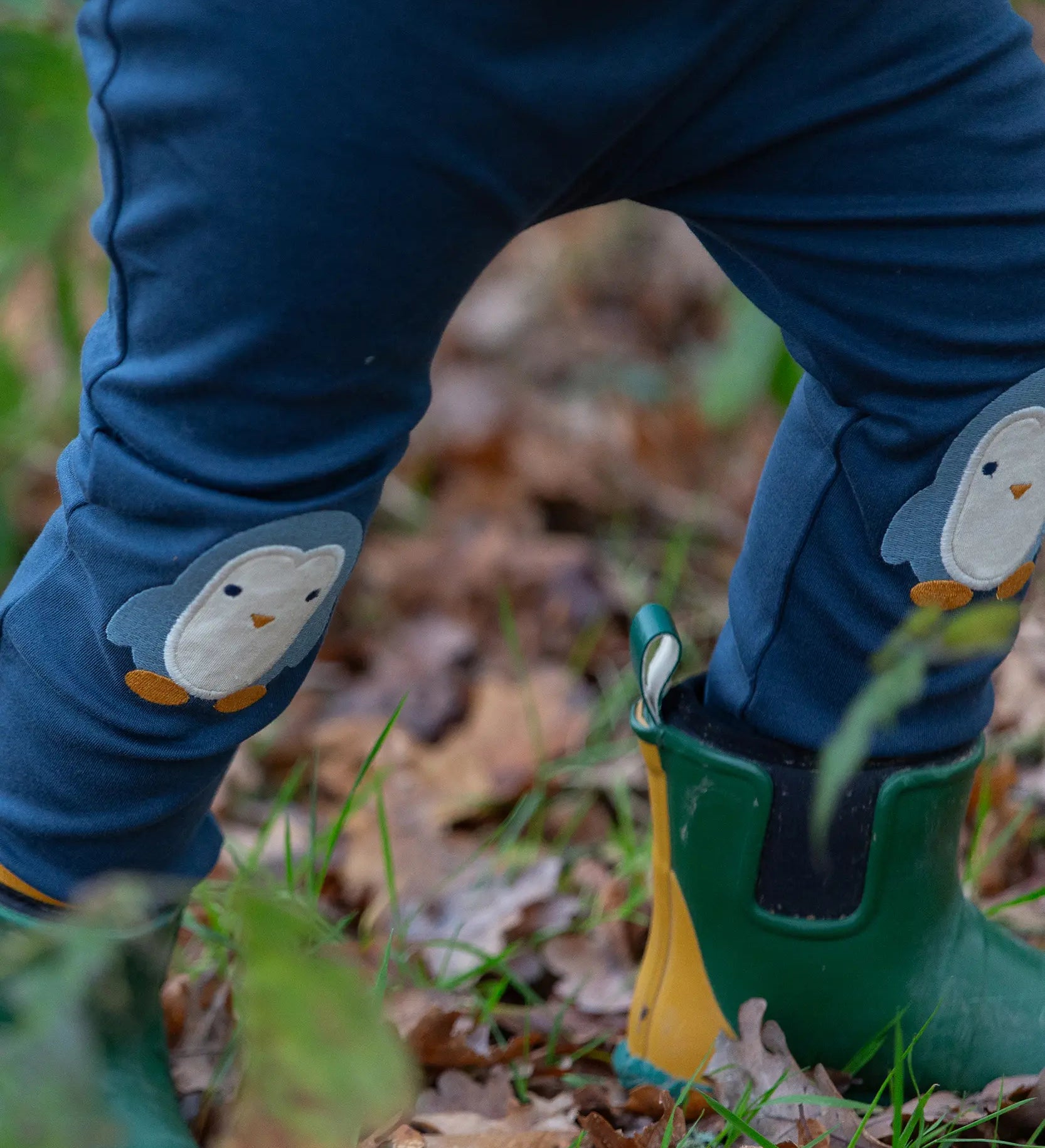 Close up of a child wearing the Little Green Radicals organic cotton knee patch joggers with a blue penguin design.