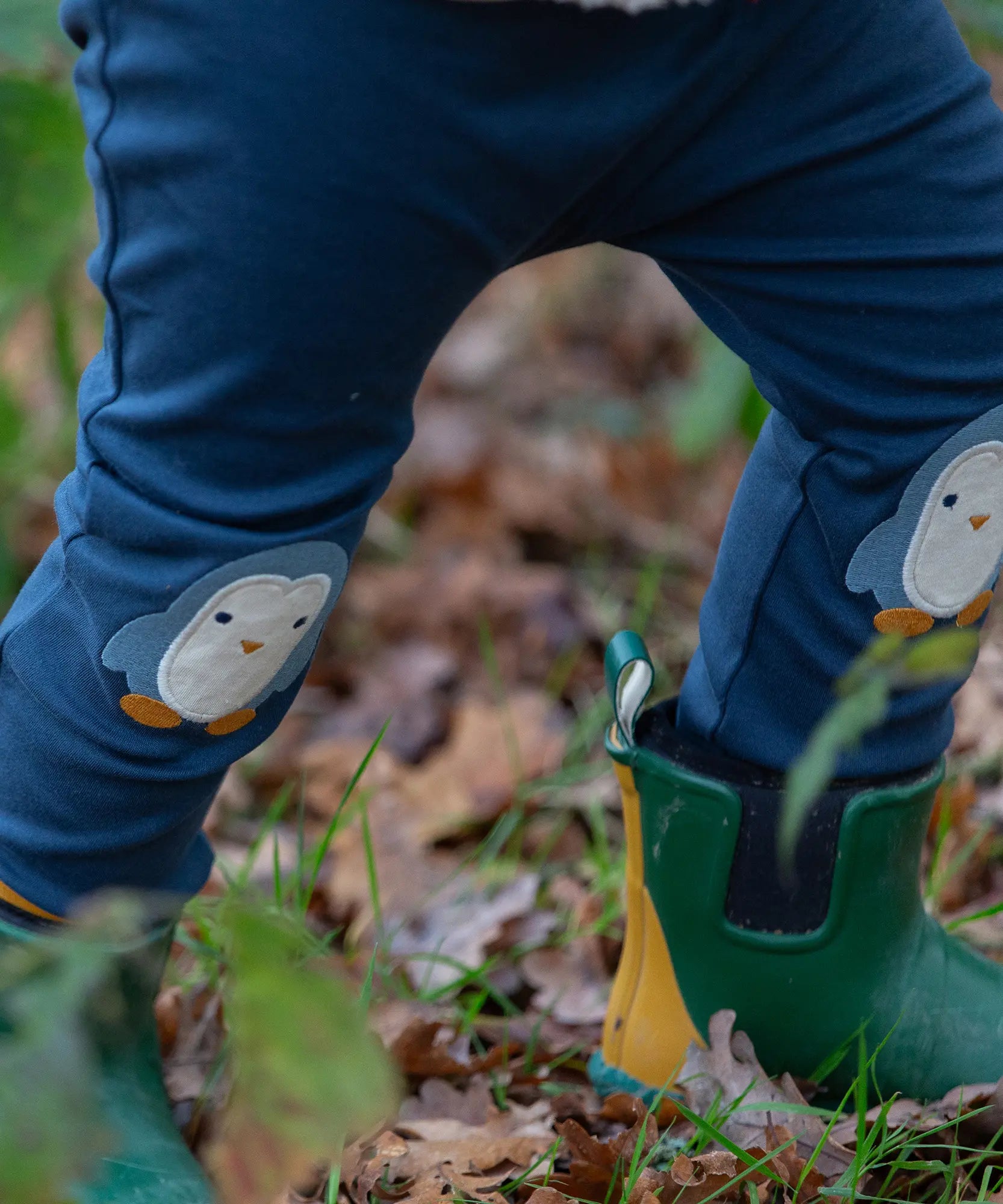 Close up of a child wearing the Little Green Radicals organic cotton knee patch joggers with a blue penguin design.