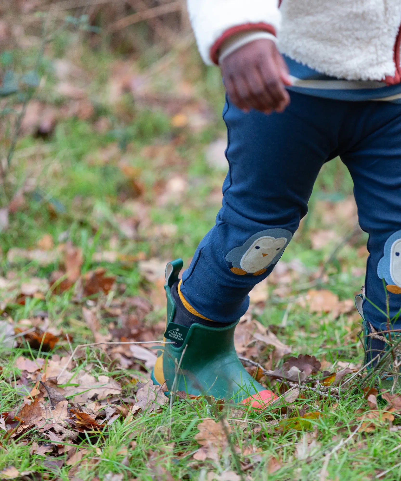 Child wearing the Little Green Radicals organic cotton knee patch joggers with a blue penguin design.