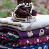 Little Green Radicals hazelnut brown organic cotton knitted baby booties placed on top of a pile of folded organic cotton knitted blankets.
