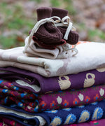 Little Green Radicals hazelnut brown organic cotton knitted baby booties placed on top of a pile of folded organic cotton knitted blankets.