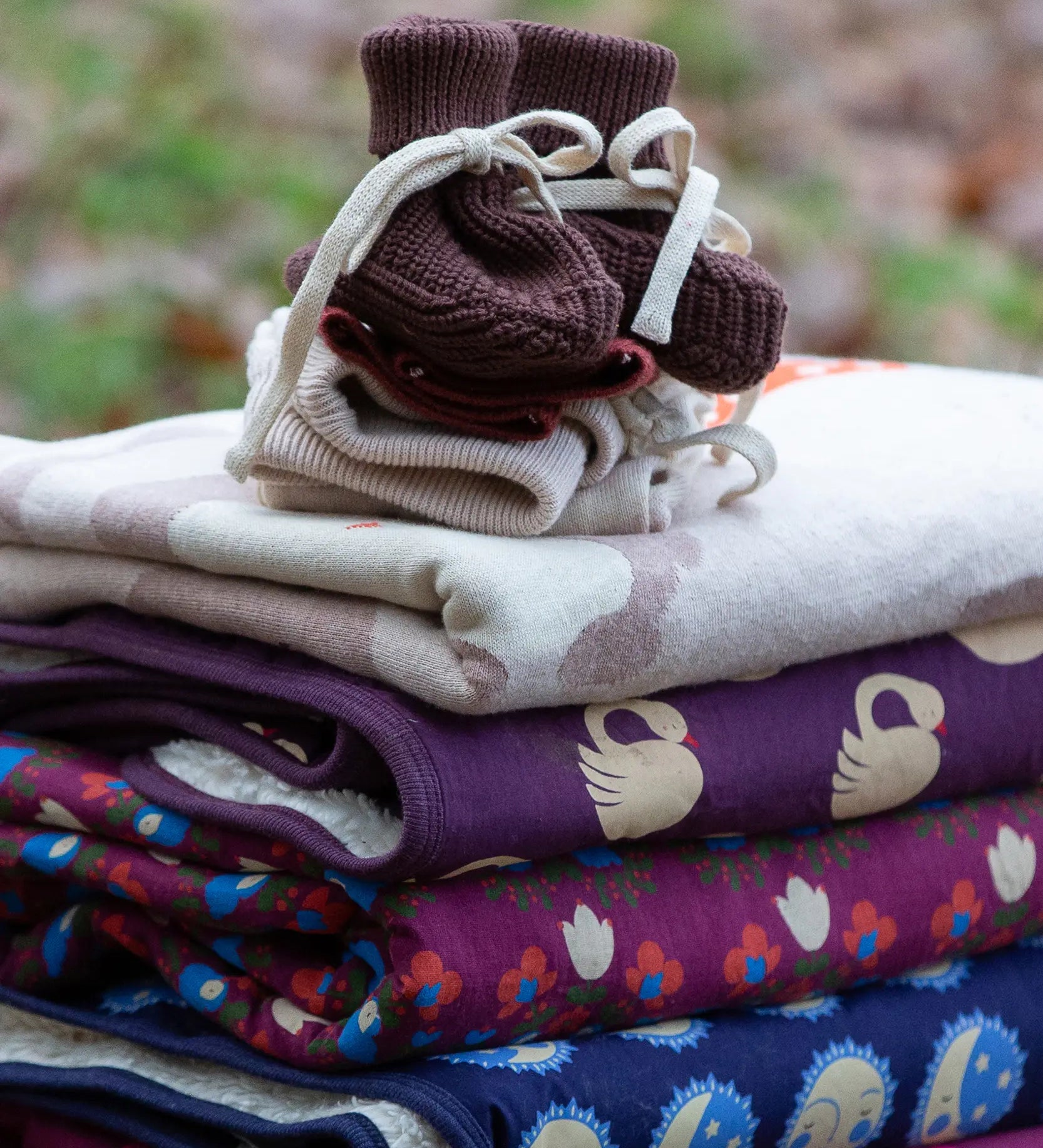Little Green Radicals hazelnut brown organic cotton knitted baby booties placed on top of a pile of folded organic cotton knitted blankets.