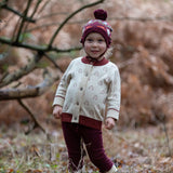 Child wearing the Little Green Radicals organic cotton knitted cardigan with snow penguins design, maroon trousers and a folk birds knitted bobble hat.