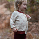 Child wearing the Little Green Radicals organic cotton knitted cardigan with snow penguins design. Natural cream cardigan with penguins all over, maroon trim on the collar and hem line.