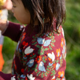 Close up of the side of a child wearing the Little Green Radicals organic cotton knitted jumper with a folk birds design with yellow gold trousers. 