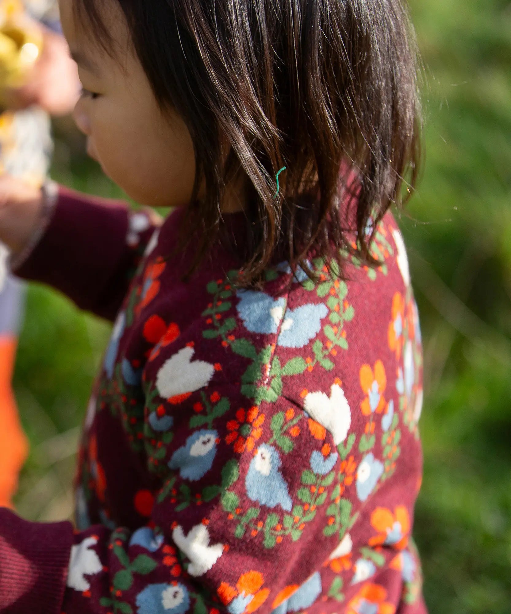 Close up of the side of a child wearing the Little Green Radicals organic cotton knitted jumper with a folk birds design with yellow gold trousers. 