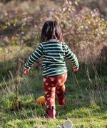 Child wearing the Little Green Radicals organic cotton knitted joggers with a mushroom design with red wellingtons and green striped long sleeved top.