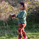 Child wearing the Little Green Radicals organic cotton knitted joggers with a mushroom design with red wellingtons and green striped long sleeved top.
