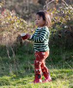 Child wearing the Little Green Radicals organic cotton knitted joggers with a mushroom design with red wellingtons and green striped long sleeved top.