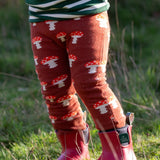 Child wearing the Little Green Radicals organic cotton knitted joggers with a mushroom design with red wellingtons. Rust orange knitted leggings featured red and white mushrooms.