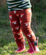 Child wearing the Little Green Radicals organic cotton knitted joggers with a mushroom design with red wellingtons. Rust orange knitted leggings featured red and white mushrooms.