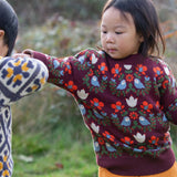 Child wearing the Little Green Radicals organic cotton knitted jumper with a folk birds design with yellow gold trousers. 
