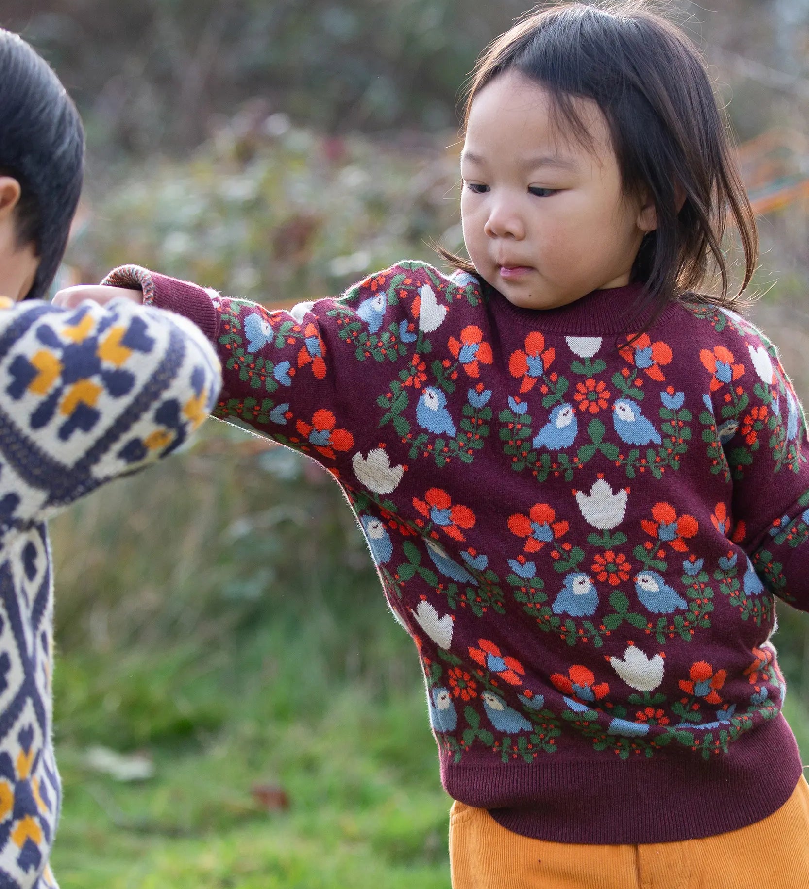 Child wearing the Little Green Radicals organic cotton knitted jumper with a folk birds design with yellow gold trousers. 