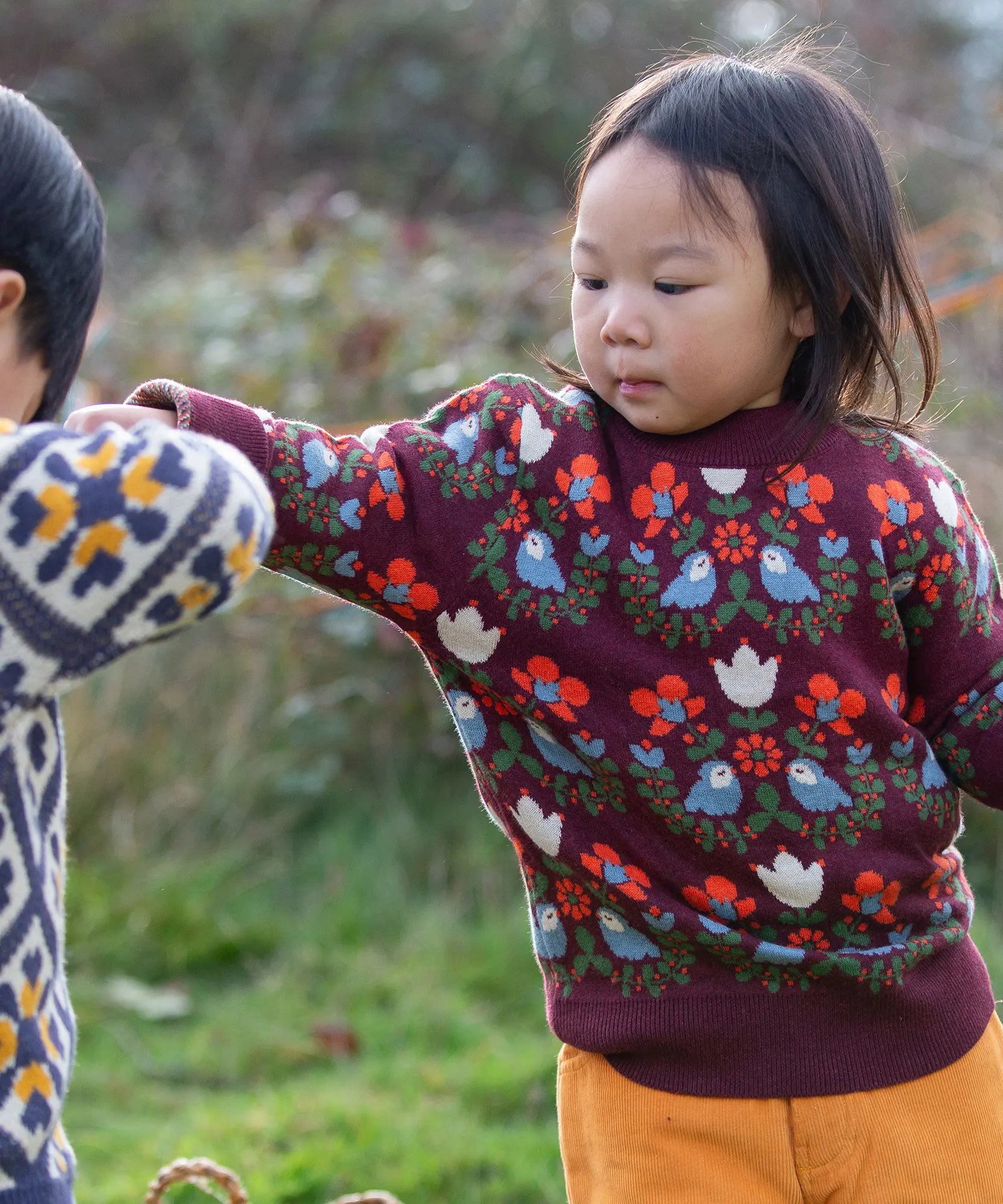 Child wearing the Little Green Radicals organic cotton knitted jumper with a folk birds design with yellow gold trousers. 