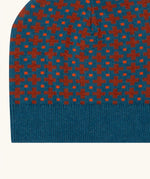 Close up of the Little Green Radicals organic cotton knitted kids beanie hat with a ginger squares design. Blue knitted hat with orange squares.
