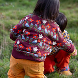 Back of a child wearing the Little Green Radicals organic cotton knitted jumper with a folk birds design with yellow gold trousers. 