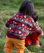 Back of a child wearing the Little Green Radicals organic cotton knitted jumper with a folk birds design with yellow gold trousers. 