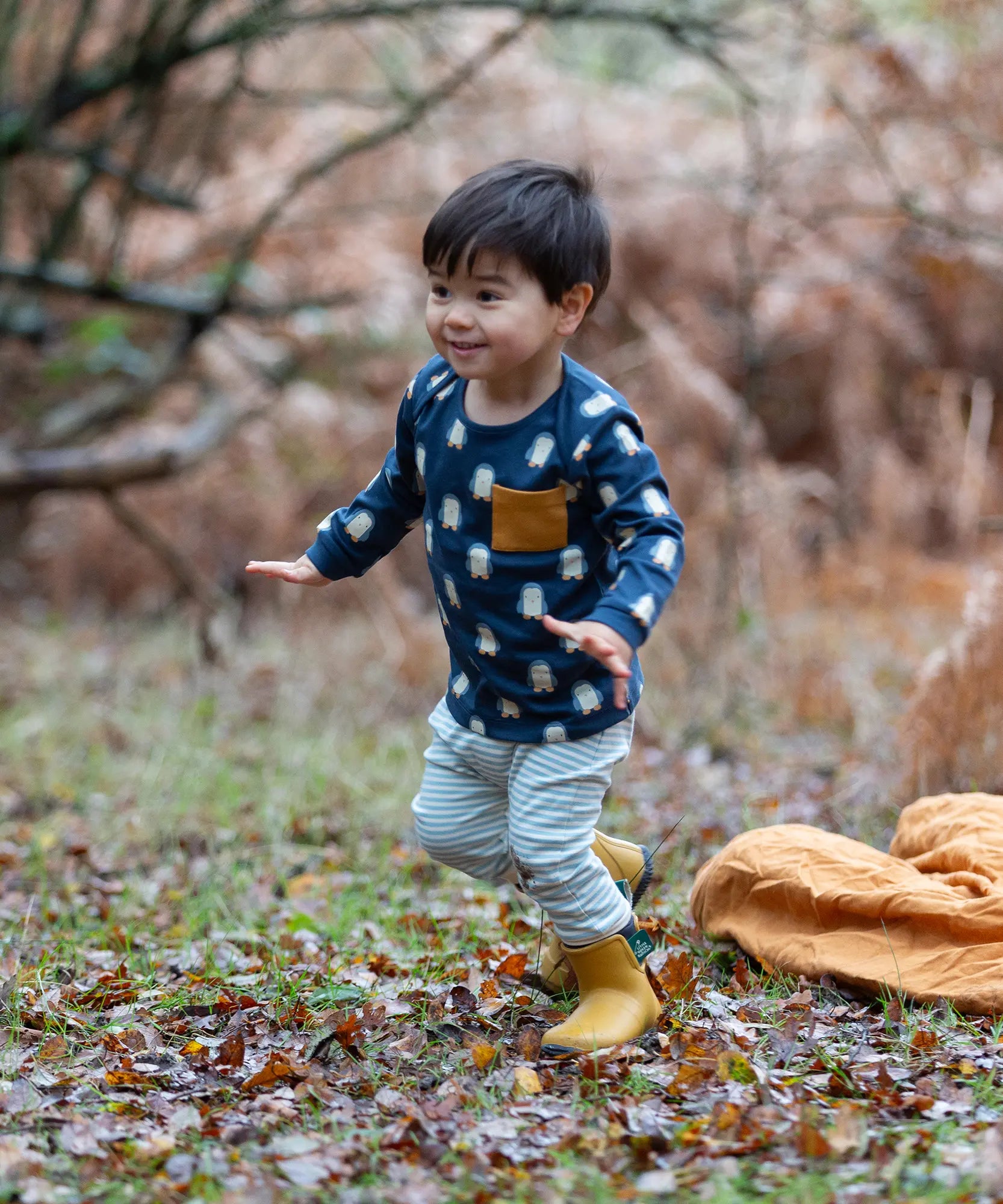 Child wearing the Little green Radicals blue penguin design playset outfit. Long sleeved organic cotton top in navy with penguins all over and light blue and white striped joggers.