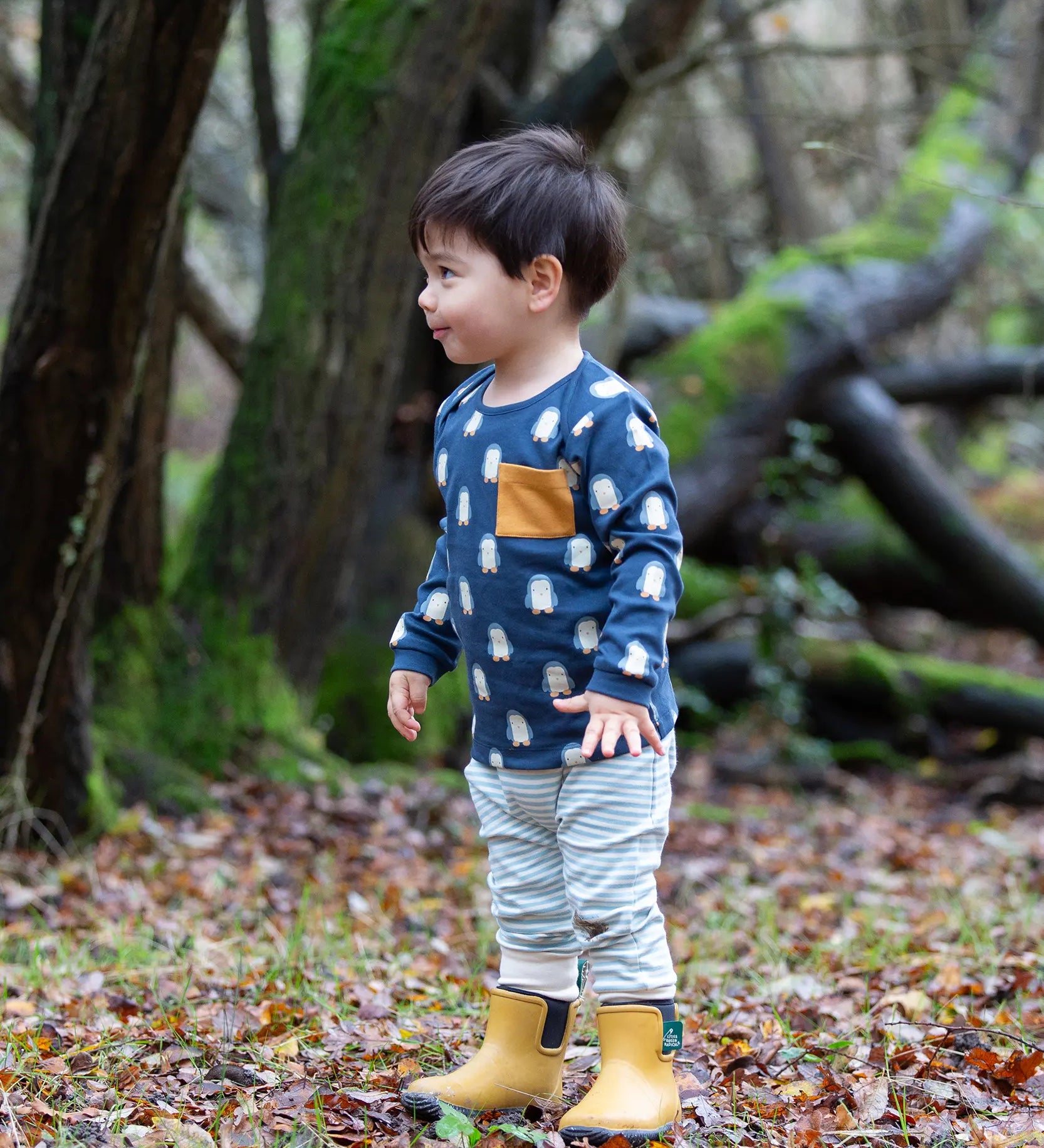 Child wearing the Little green Radicals blue penguin design playset outfit. Long sleeved organic cotton top in navy with penguins all over and light blue and white striped joggers.