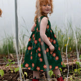 Side of the Little Green Radicals green orange blooms repeat print reversible pinny kids dress being worn with red wellington boots.