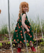 Side of the Little Green Radicals green orange blooms repeat print reversible pinny kids dress being worn with red wellington boots.