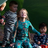 Children standing outside a tent in the forest. They are all wearing Little Green Radicals organic ccotton pyjamas. One is wearing a pair with the Winter Rabbit on them, one in wearing navy and white striped design and the third is wearing the sleeping sheep print. Little green Radicals have a wide range of organic cotton, Fairtrade children's clothing an outerwear available here at Babipur.