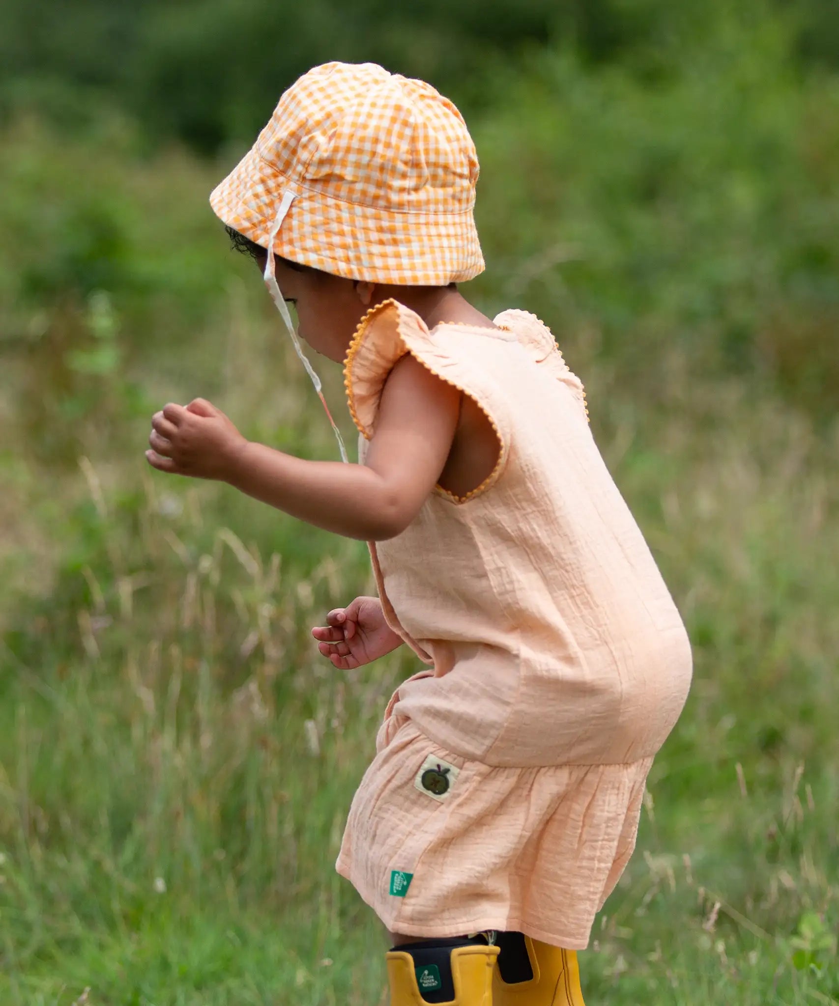  Little Green Radicals organic cotton reversible Flora sunhat with a yellow and white gingham design on a child. View of back.