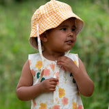 Child wearing the Little Green Radicals organic cotton reversible Flora sunhat with a yellow and white gingham design.