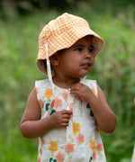 Child wearing the Little Green Radicals organic cotton reversible Flora sunhat with a yellow and white gingham design.