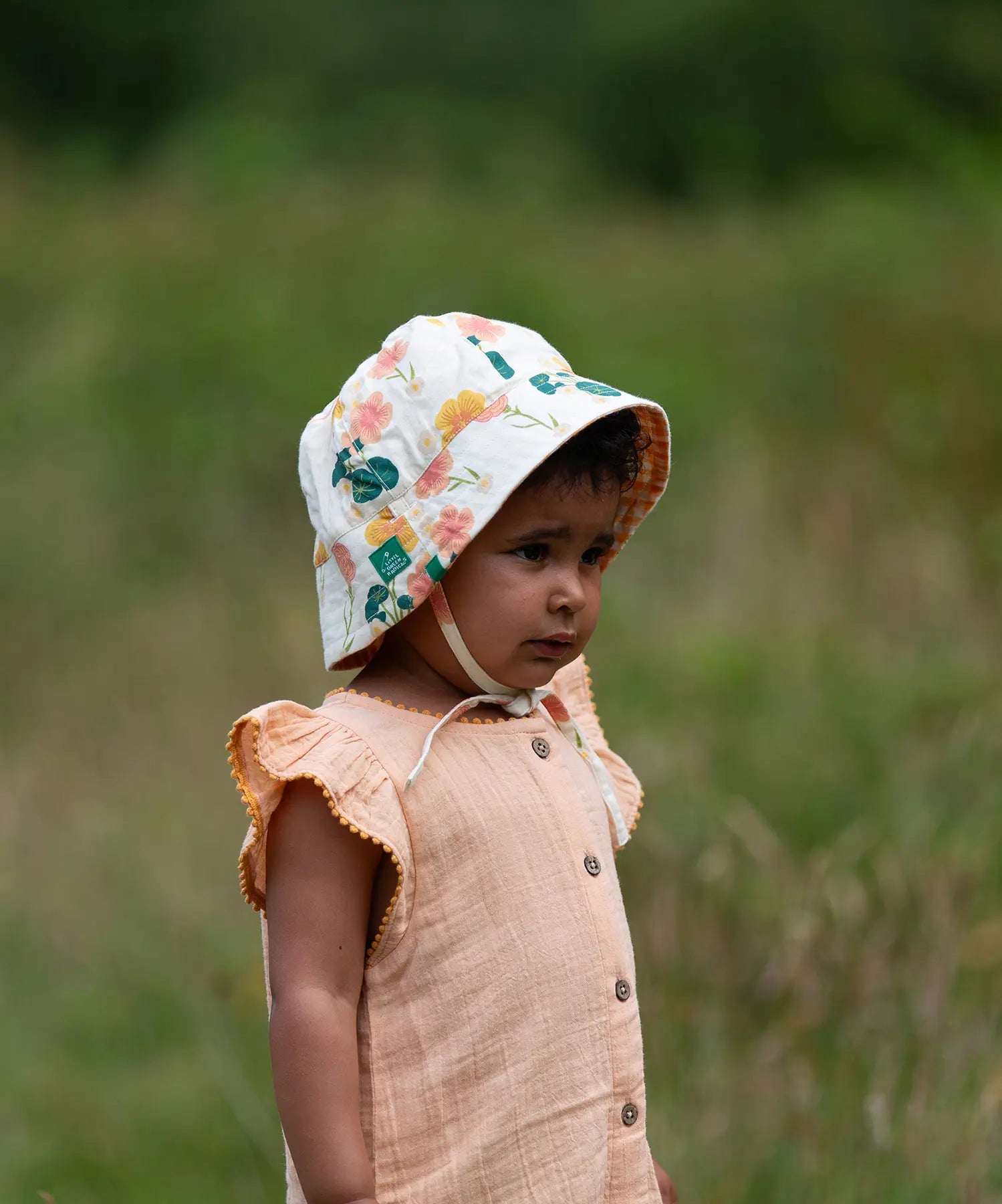 Child wearing the Little Green Radicals organic cotton reversible sunhat on the flora pink and yellow flowers print side.