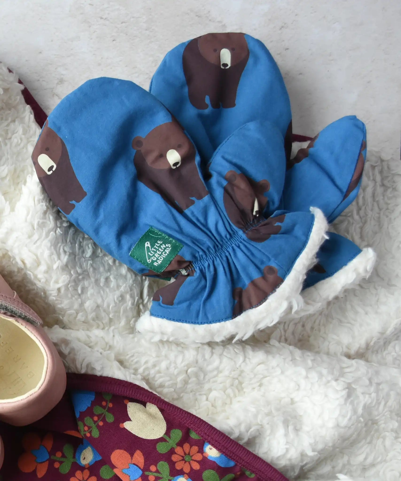 Little Green Radicals Organic Cotton Sherpa-Lined Children's bear print mittens placed on a sherpa lined blanket.